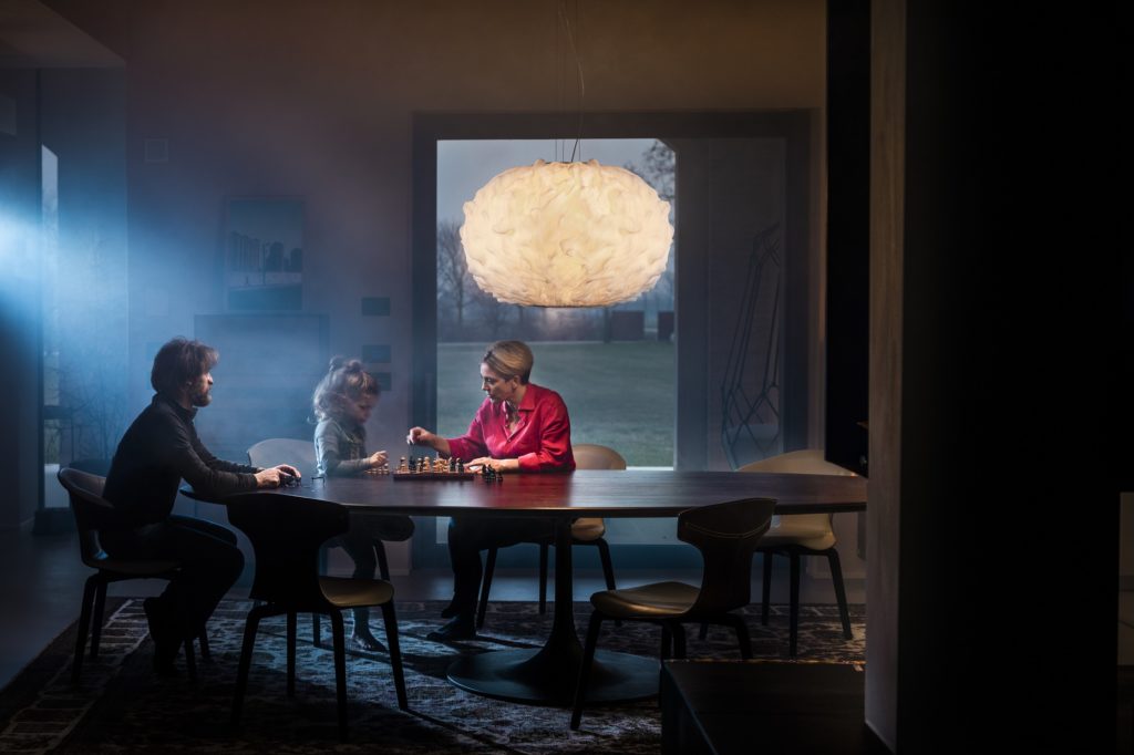 a family playing chess at the kitchen table with the Nuée light in the background