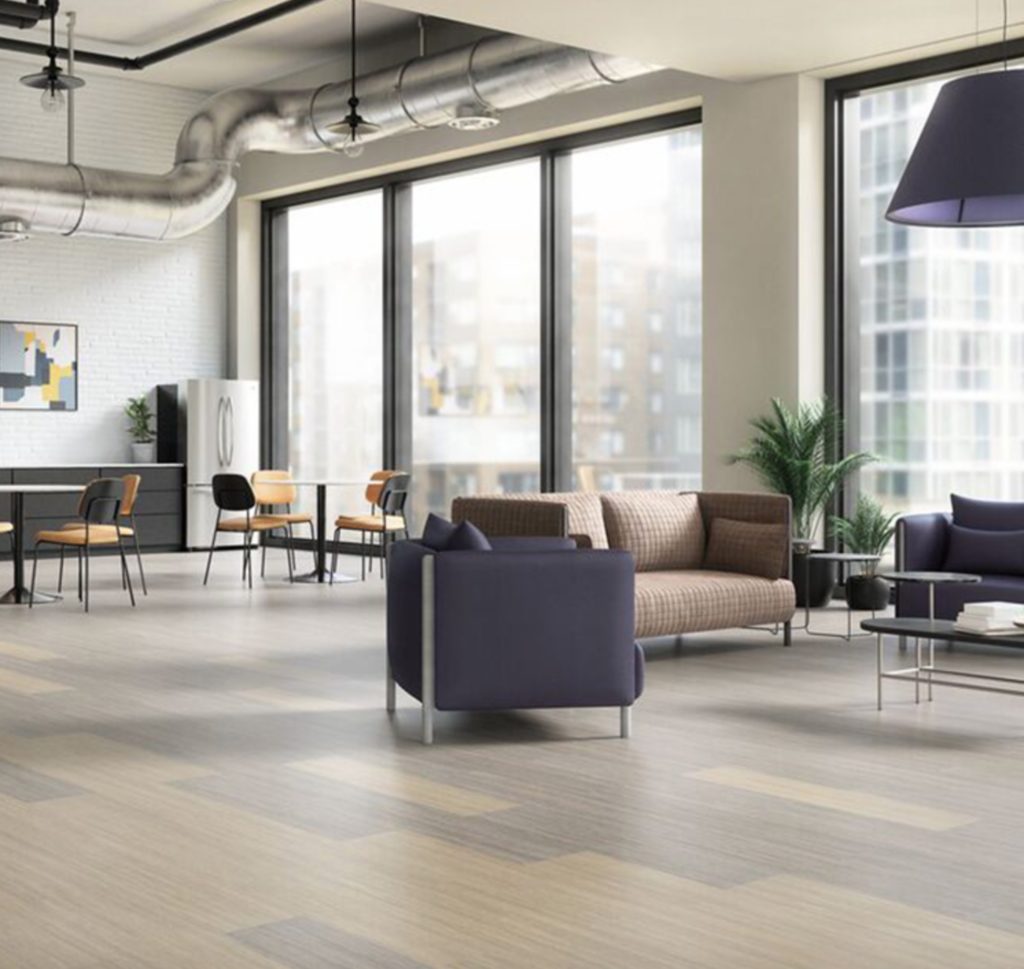 Natural wood LVT strips in open workspace with cafe tables, lounge chairs, and sofa