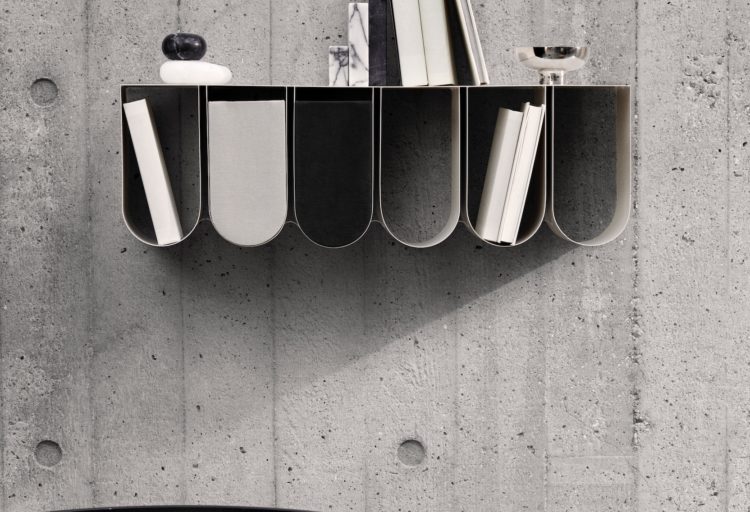 Curved wall shelf in black with many items on a concrete wall
