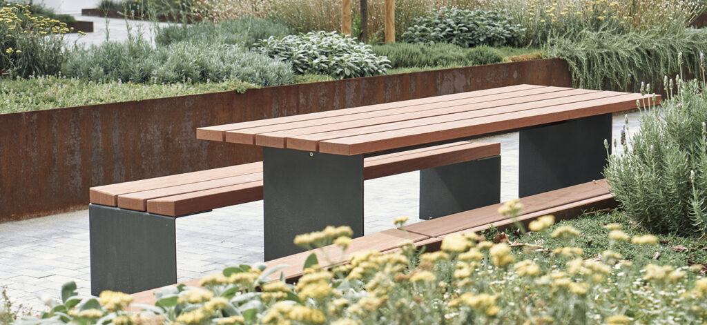 Bancal Table and Bench on walkway flanked by verdant plantings