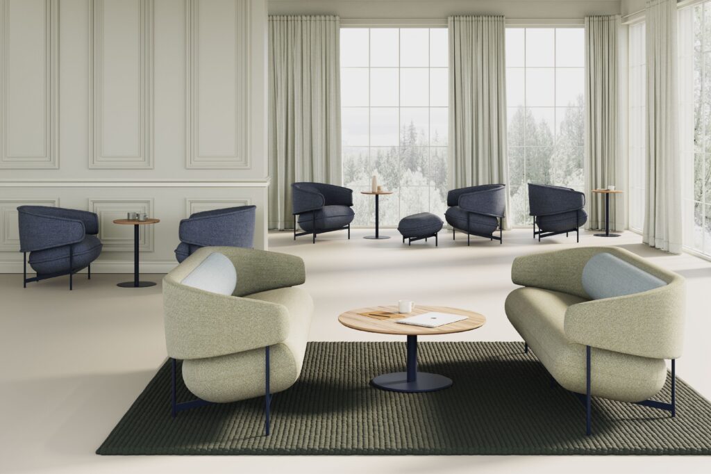 Sofas and lounge chairs in off-white and medium-dark blue in open space with white curtains and windows looking out onto trees