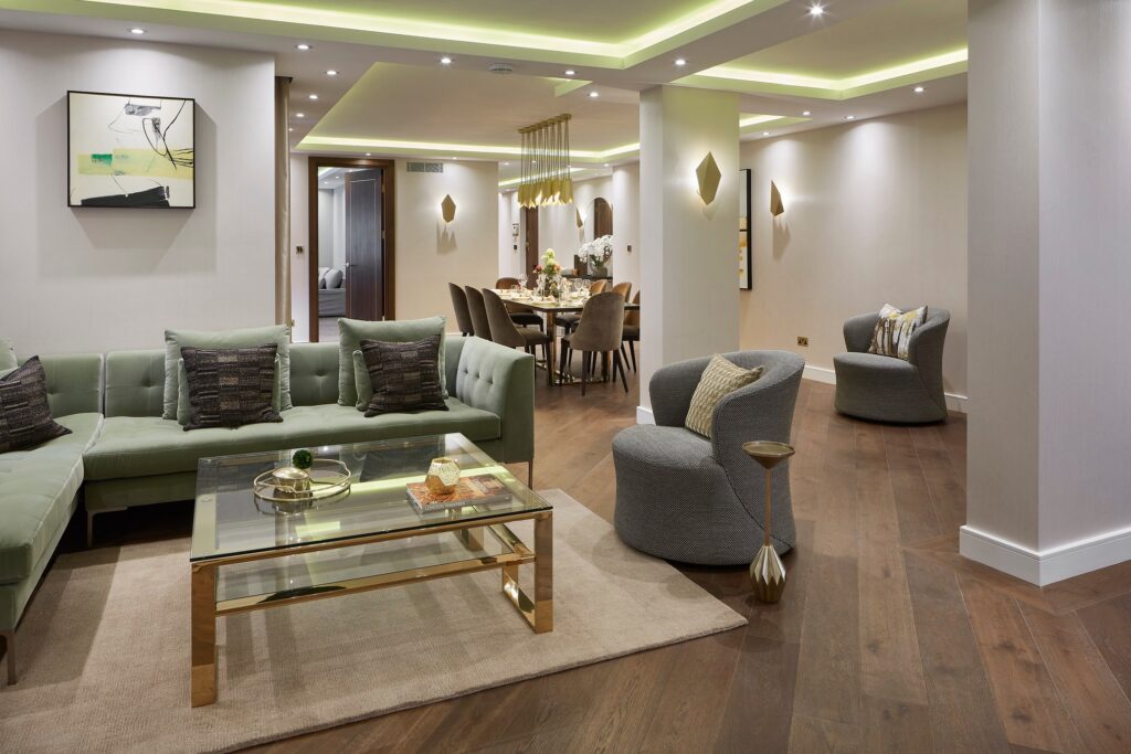 a room in a London penthouse with mint green modular sofa, two gray lounge chairs and square coffee table atop rug and dark oak wood flooring