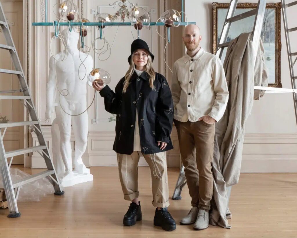 Jackson Schwartz and Victoria Sass posing with Ontologia chandelier in the background