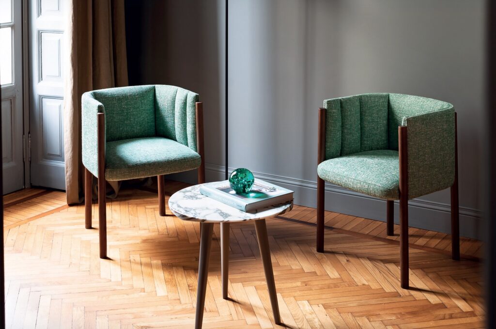 Two Baia chairs in greenish/blue color on herringbone wood floor with circular table. 