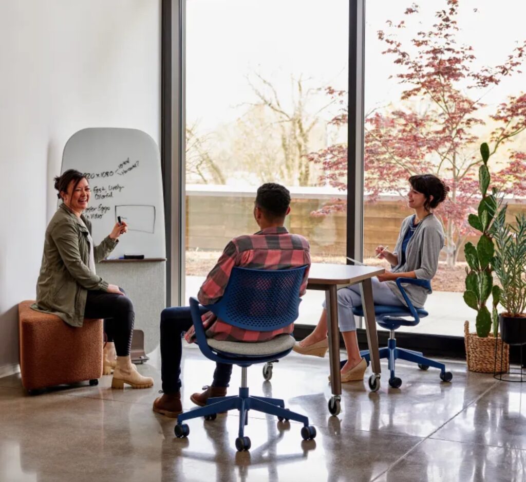 Three people discussing whiteboard notes while sitting in blue Picado task chairs