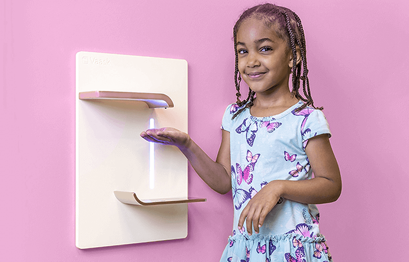 Little girl dispensing hand sanitizer with pink wall backdrop