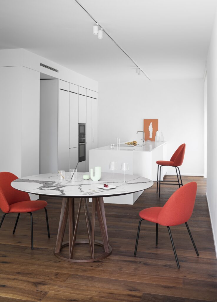 ACCO table in compact kitchen with ceramic top, medium-toned wood base, and red upholstered chairs