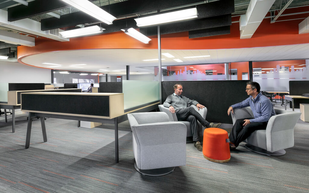 MÜM in orange in office space with two men talking