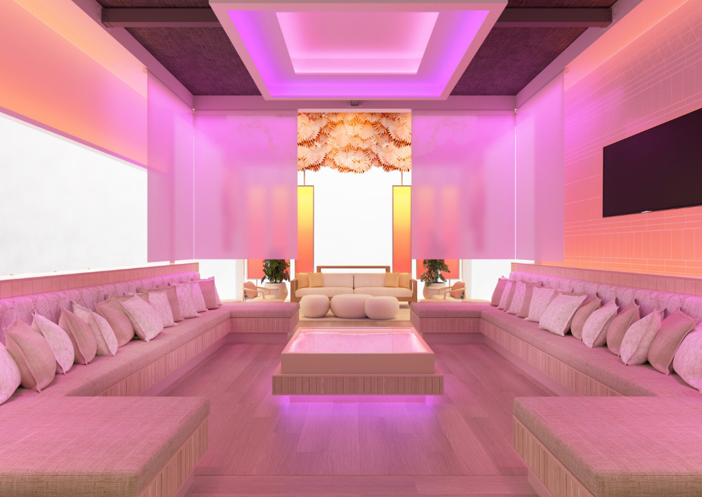 Room with wall-to-wall sofas and pillows with pinkish/red light suffused throughout to duplicate the sunset