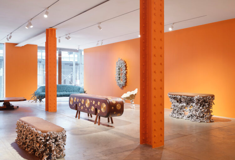 On the road exhibit with several pieces of furniture in open exhibition space with orange pillars