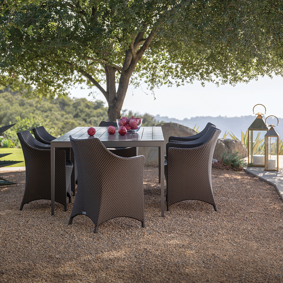 Rectangular dining table with comfy mesh armchairs in the shade of a tree