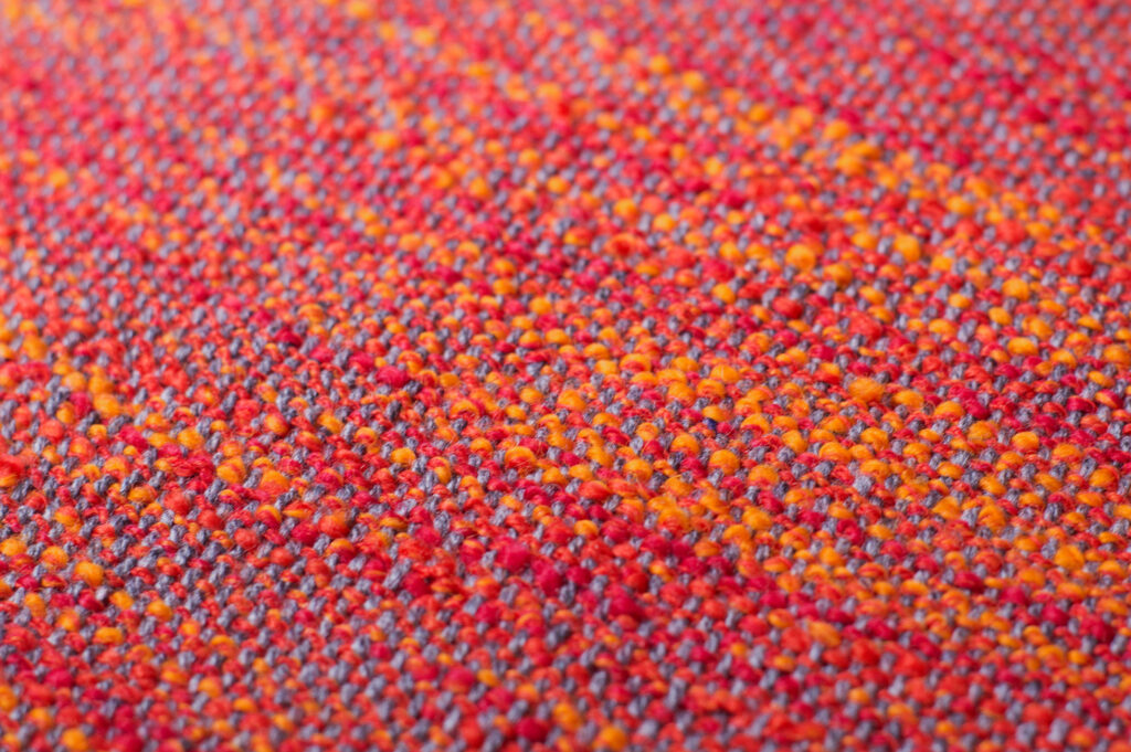 textile detail: reds and oranges with blue stitching woven in