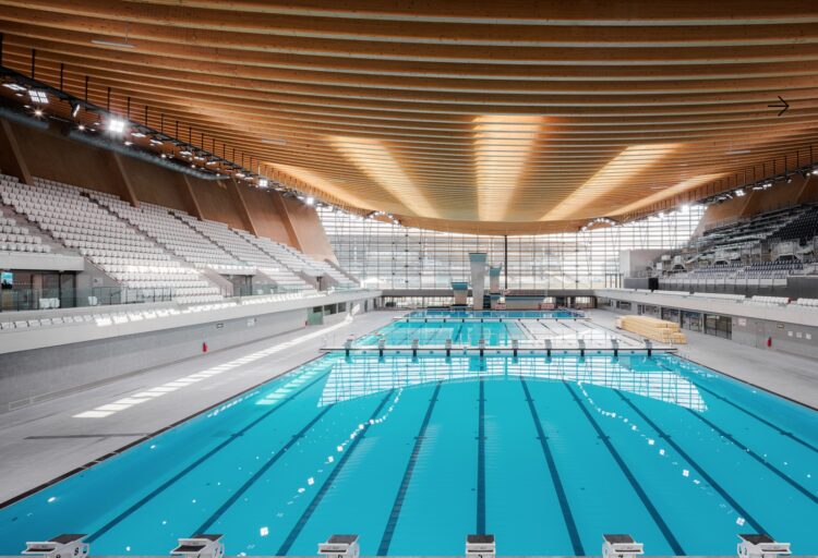 Interior of Paris Aquatics Center with view of pool and timber roof