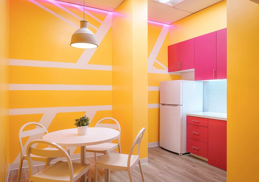 Reach L.A. pantry with yellow walls painted with white geometric shapes, café table, and hot pink cabinets