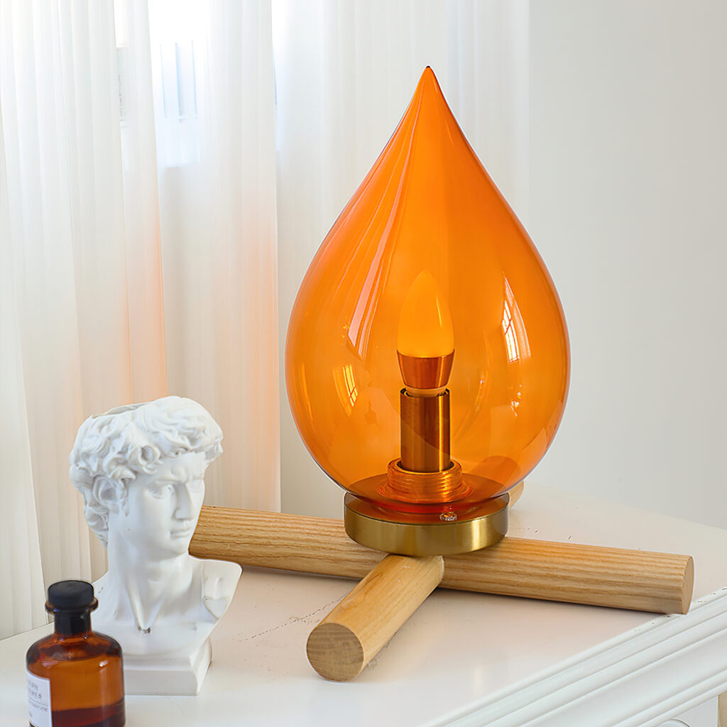 Table lamp with an orange bulb shaped like an inverted teardrop next to a small Greek bust