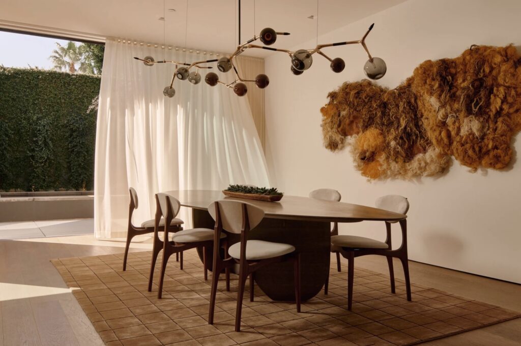 Pebble dining table, femur chairs, ornate modern chandelier, wooly rug on wall in nice dining room