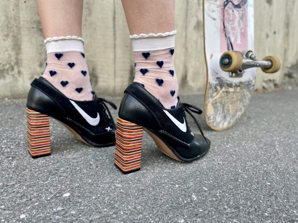 High heel shoes in black with Nike swoosh worn by woman holding skateboard